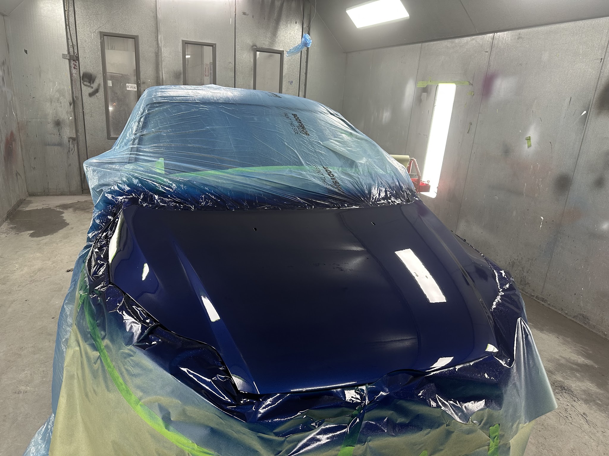 Blue car masked for paint inside a spray booth.